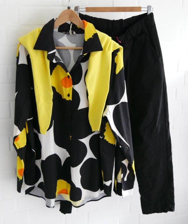 Schwarze Hose mit bunter Oversize Bluse und gelbem Pullover über Schulter